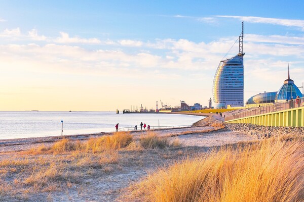 Das Bild zeigt einen Strand und Wasser im Vordergrund sowie ein segelförmiges Gebäude am Horizont | © Tim Mrzyglod auf Pixabay